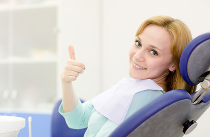 A smiling patient gives a thumbs up while seated in a chair at the dentist.