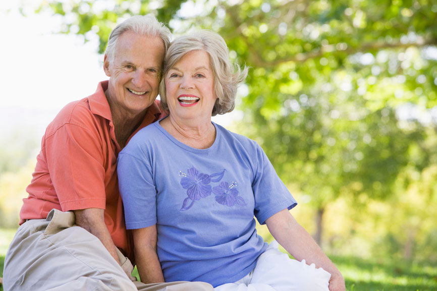 A senior couple sits together outdoors, smiling.